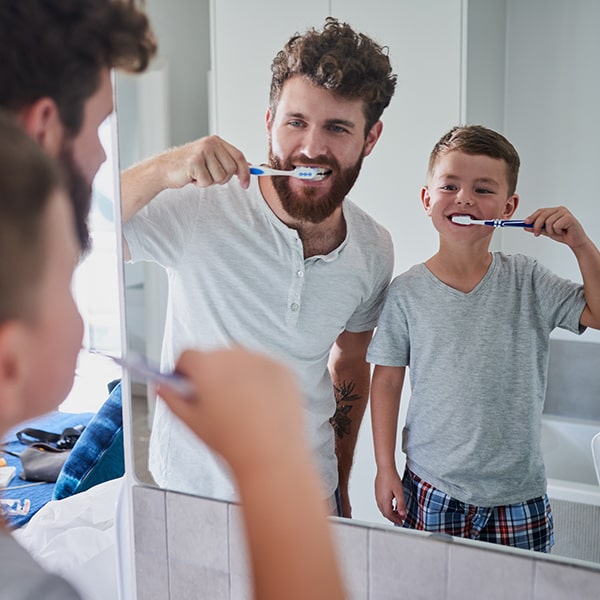 A father brushing his teeth with his son in front of the mirror