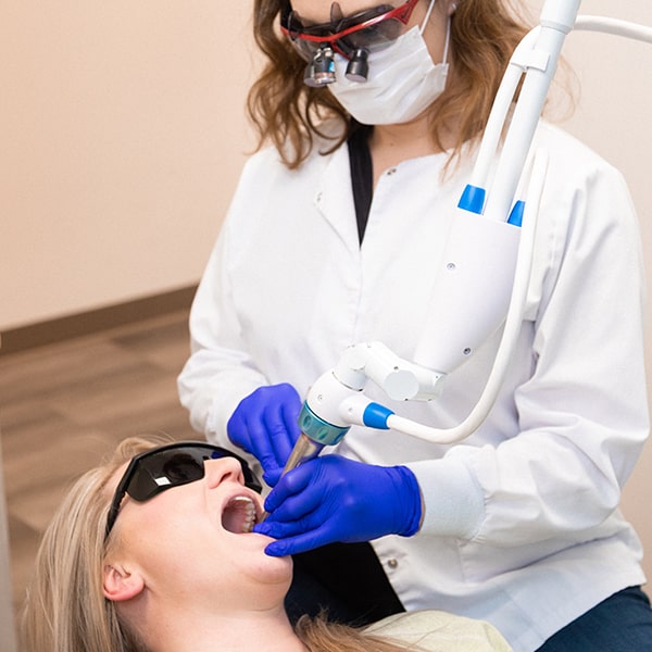Dr. Kristy Gretzula using a SOLEA laser machine in the mouth of a woman who is lying in the dentist's chair