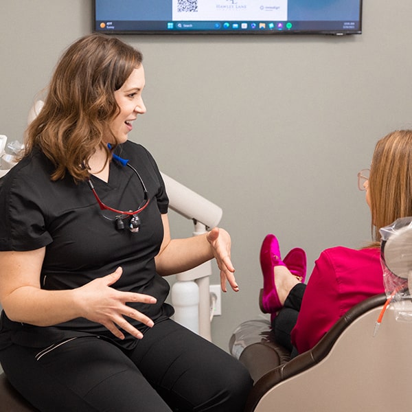 Dr. Kristy Gretzula talking about TMJ symptoms with a woman sitting in the dentist's chair