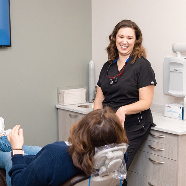 Dr. Kristy Gretzula explaining to a woman lying in the dentist's chair about the process of dental bridges