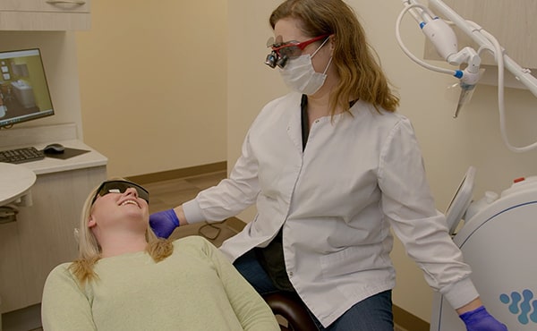 Video thumbnail showing a young woman in the dentist's chair smiling next to Dr. Kristy Gretzula after her laser treatment
